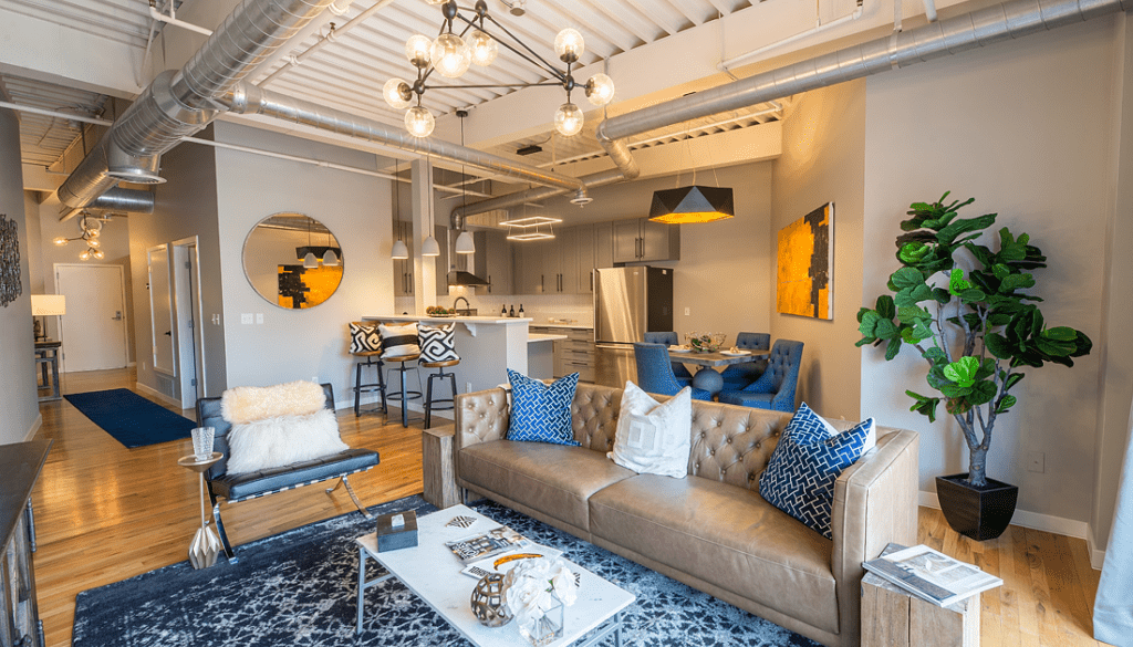 Interior Design of a Cozy Living Room with a Couch, Chairs, Table, Refrigerator, and a Room Plant in a Corner, featuring Good Lighting by Woodmax Interior Designers in Mangalore