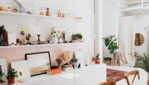 Interior design by Woodmax featuring a room with a wall-mounted shelf containing books, chairs, a mirror, a room plant, and white curtains.