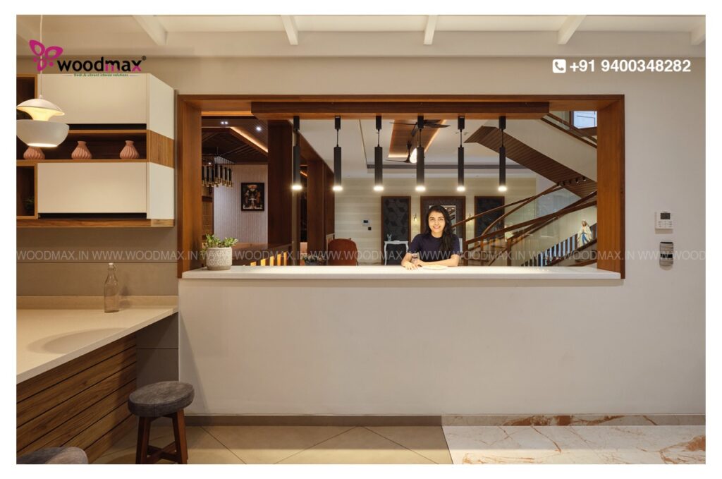 In the modern home interior designed by Woodmax in Kasaragod, Kannur, and Mangalore, Kerala, a woman is standing and admiring the hanging light.